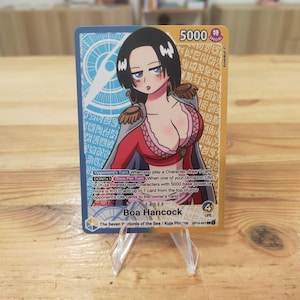 Könnte beinhalten: Sammelkarte mit einer Anime-Illustration von Boa Hancock. Die Karte hat einen blauen und goldenen Hintergrund mit japanischem Text und einer Stärke von 5000. Hancock ist in einem rot-rosa Outfit dargestellt.