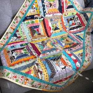 May include: A multicolored patchwork quilt featuring a variety of fabric patterns including animals, geometric shapes, and stripes. The quilt is constructed from numerous small fabric strips arranged in a star-like pattern with a teal border.