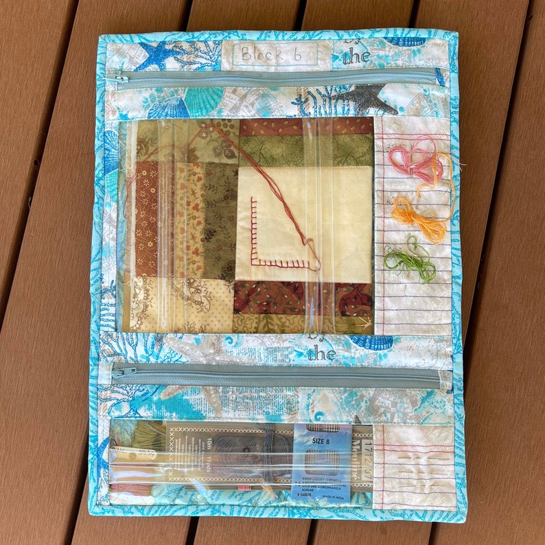 May include: A blue fabric project bag with a clear plastic window showing a patchwork quilt block. The bag has a zipper closure and a label that says "Block 6". There are also several spools of embroidery floss and a package of needles inside the bag.