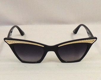 Könnte beinhalten: Schwarze Cat-Eye-Sonnenbrille mit goldenen Akzenten am Rahmen.