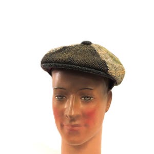 May include: A brown, green, and tan tweed newsboy cap with a dark brim and a small button on top. The cap is displayed on a mannequin head with a neutral skin tone and rosy cheeks.