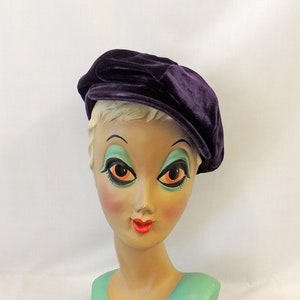 May include: A purple velvet beret with a bow on top. The beret is on a mannequin head.