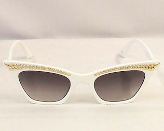 Könnte beinhalten: Weiße Cat-Eye-Sonnenbrille mit goldfarbenen Akzenten am Rahmen.