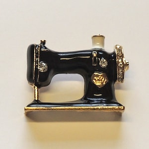 May include: A black and gold sewing machine brooch with rhinestones. The sewing machine is a popular motif for jewellery and is a great gift for crafters and sewers.