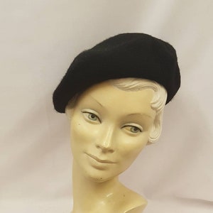May include: A black beret made of wool, worn on a mannequin head.
