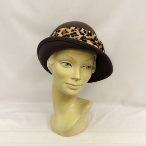 May include: A brown felt cloche hat with a leopard print ribbon.