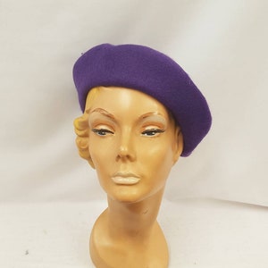 May include: A purple beret made of felt. The beret is sitting on a mannequin head.