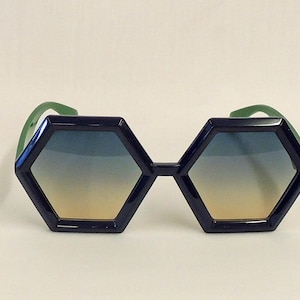 May include: A pair of hexagonal sunglasses with a blue and yellow gradient lens and green arms.
