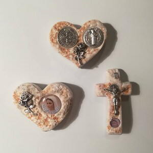 K&ouml;nnte beinhalten: Drei herzf&ouml;rmige Steinschmuckst&uuml;cke mit religi&ouml;sen Motiven. Das erste Herz zeigt eine silberne St. Christopher-Medaille und eine silberne St. Benedikt-Medaille. Das zweite Herz zeigt eine silberne Rose und ein Bild der Jungfrau Maria mit dem Text "Medjugorje". Das dritte Herz ist ein Kreuz mit einer silbernen Jesusfigur.