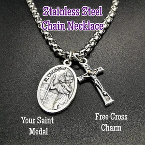 May include: Stainless steel chain necklace with a silver St. Christopher medal and a silver cross charm. The medal features a depiction of St. Christopher carrying a child. The cross charm has a figure of Jesus on it.