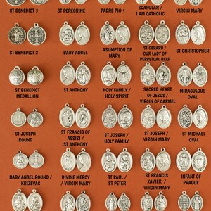Pu&ograve; includere: Una collezione di medaglioni in metallo argentato con varie figure e simboli religiosi. I medaglioni sono disposti in file su uno sfondo marrone. I medaglioni includono immagini di San Benedetto, Sant'Antonio, San Giuseppe, San Francesco d'Assisi, San Michele, la Vergine Maria, il Sacro Cuore di Ges&ugrave;, e altro ancora.