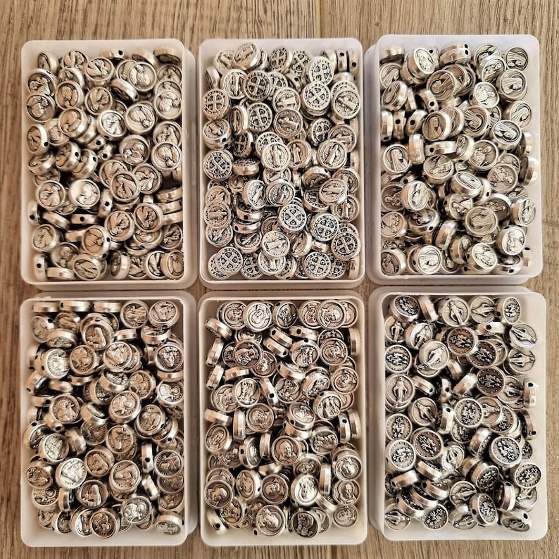 May include: Six clear plastic containers filled with silver metal beads. Each bead has a raised design of a religious figure or symbol.