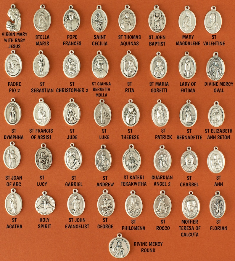 Pu&ograve; includere: Una collezione di medaglioni religiosi ovali in argento con vari santi e figure cattoliche. I medaglioni sono disposti in file su uno sfondo marrone.