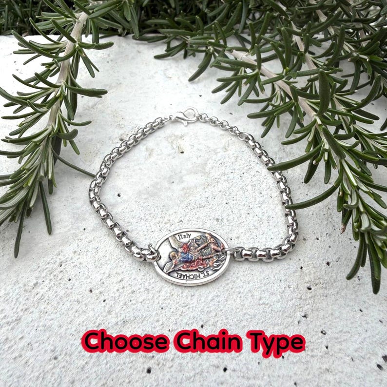 Puede incluir: Una pulsera de plata con un colgante ovalado detallado que presenta una escena religiosa y la palabra "Italy". La pulsera tiene un dise&ntilde;o de eslabones de cadena y se muestra sobre una superficie blanca con follaje verde. El texto "Choose Chain Type" est&aacute; en la parte inferior.