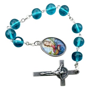 May include: A teal blue rosary with a silver crucifix and a silver oval charm featuring a picture of Saint Lucy. The charm has the text "St. Lucy" on it.