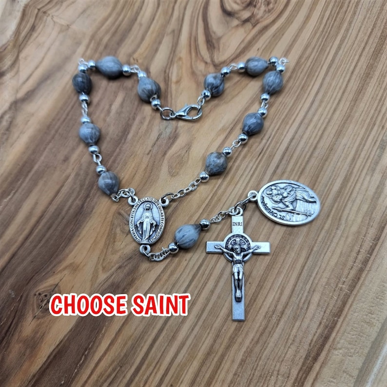 May include: A silver rosary with grey wooden beads, a silver crucifix, and a silver medal of Saint Jude Thaddeus. The text "CHOOSE SAINT" is visible below the rosary.