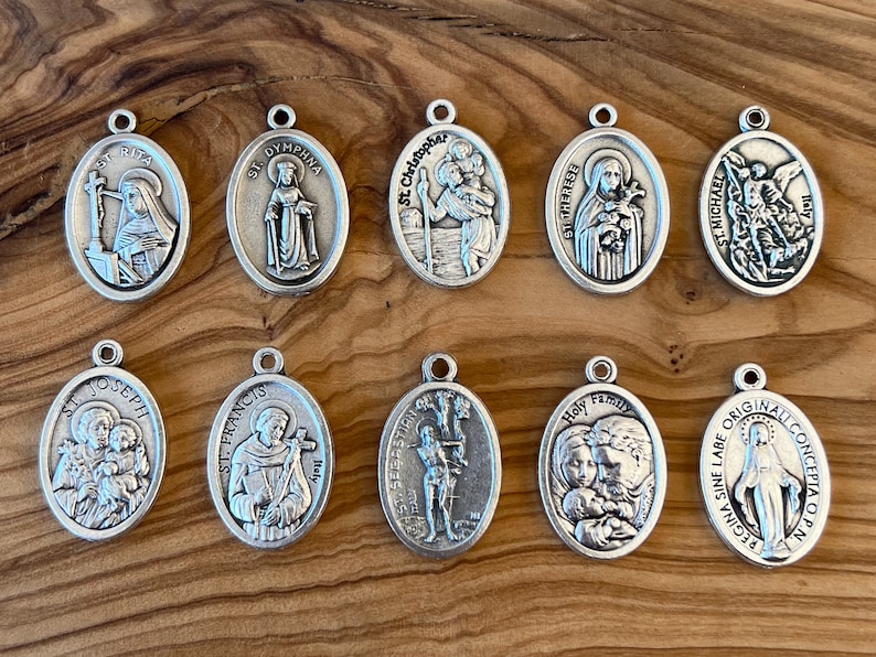 May include: Ten silver oval-shaped pendants with religious imagery. Each pendant features a different saint or religious figure, including St. Joseph, St. Francis, St. Sebastian, St. Dymhpna, St. Christopher, St. Therese, the Holy Family, and the Virgin Mary.