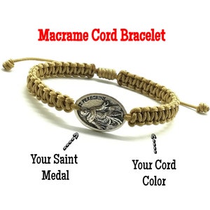May include: A brown macrame cord bracelet with a silver oval medal featuring a depiction of Saint Peregrine. The medal is attached to the bracelet with a knot.