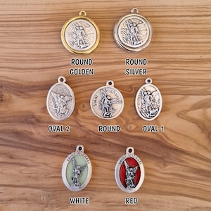 May include: Six different Saint Michael medallions, each with a different color and design. The medallions are round and oval shaped, with a silver finish. The medallions feature a depiction of Saint Michael, the archangel, with a sword and shield. The medallions are labeled with the colors: golden, silver, oval 2, round, oval 1, white, and red.