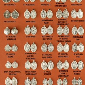 May include: A collection of 25 silver oval-shaped medallions with various religious figures and symbols. The medallions are arranged in five rows of five. Each medallion has a different image, including St. Benedict, St. Anthony, St. Joseph, St. Francis, St. Michael, the Virgin Mary, and the Sacred Heart of Jesus.