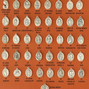 May include: A collection of 36 silver oval-shaped charms featuring religious figures and symbols. The charms are arranged in rows on a brown background. The charms include images of saints, angels, and religious figures such as the Virgin Mary, St. Francis, and St. John the Evangelist.
