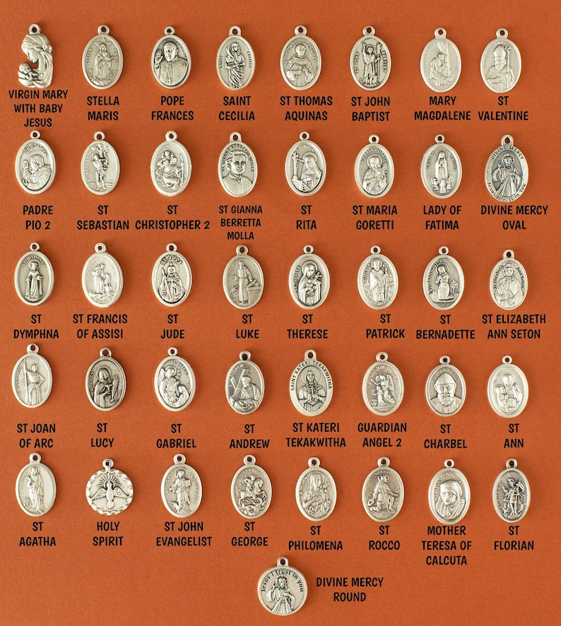 May include: A collection of 36 silver oval-shaped charms featuring religious figures and symbols. The charms are arranged in rows on a brown background. The charms include images of saints, angels, and religious figures such as the Virgin Mary, St. Francis, and St. John the Evangelist.