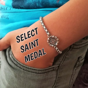 May include: A silver chain bracelet with a silver flower charm featuring a Saint medal. The text "SELECT SAINT MEDAL" is superimposed on the image.