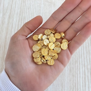 Könnte beinhalten: Eine Hand hält einen Haufen goldfarbener Metallperlen mit einem erhabenen Design. Die Perlen sind rund und haben eine leicht strukturierte Oberfläche.