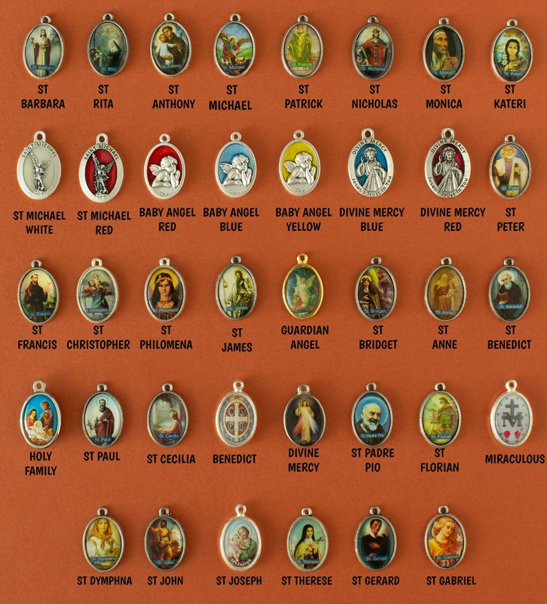 May include: A collection of 36 oval-shaped metal charms with various religious figures and images. The charms are silver, gold, and red with colorful images of saints, angels, and religious symbols. The charms are arranged in rows on a brown background.