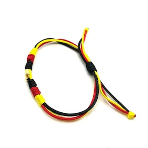 May include: A black, red, and yellow braided bracelet with a gold bead accent.