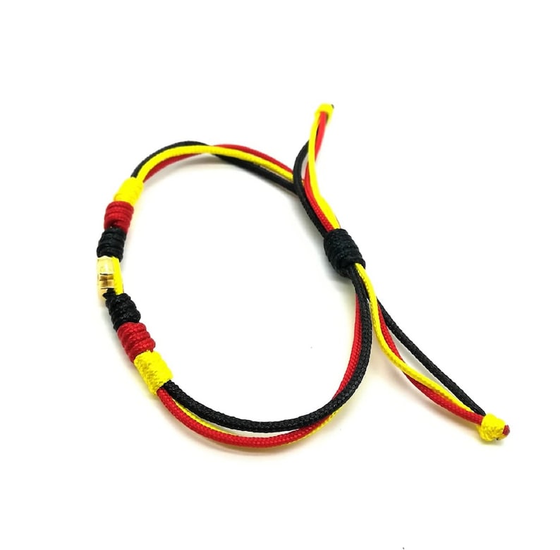 May include: A black, red, and yellow braided bracelet with a gold bead accent.
