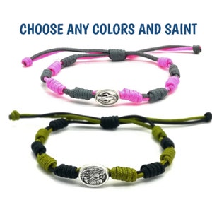 May include: Two adjustable bracelets with knotted cords and a silver charm. The top bracelet is pink and gray, and the bottom bracelet is green and black.  "CHOOSE ANY COLORS AND SAINT" is written in blue text at the top of the image.
