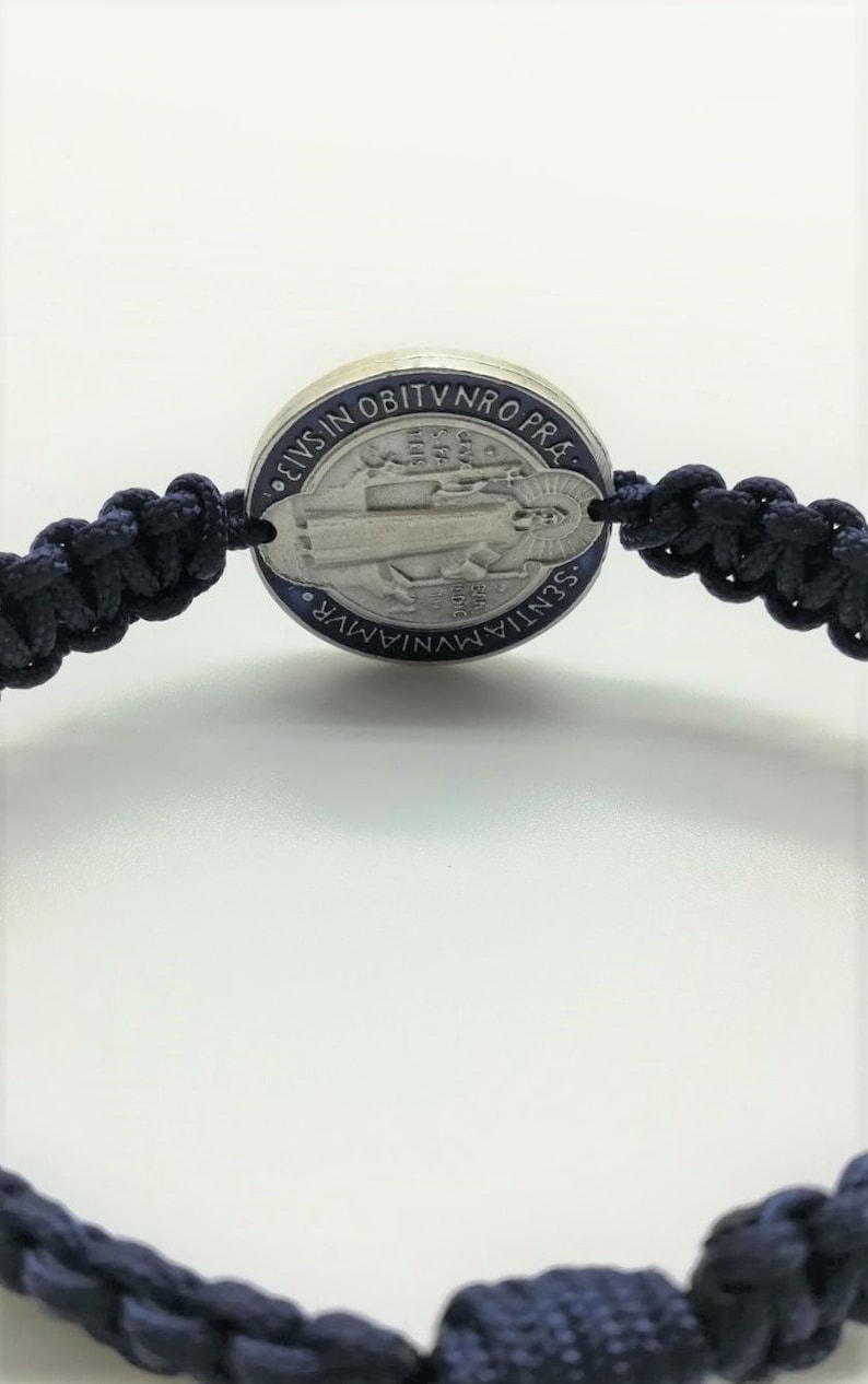 Pu&ograve; includere: Un braccialetto intrecciato blu con un ciondolo d'argento raffigurante la Vergine Maria. Il ciondolo ha il testo "S. MARIA.  M.V.N.I.A.R.  S.S.N.T.I.A.  O.B.I.T.V.N.R.O.P.R.A." attorno al bordo.