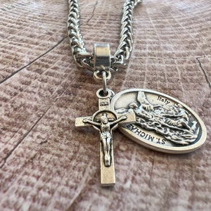 May include: Silver chain necklace with a silver cross pendant and a silver St. Michael medal pendant. The medal has the words "St. Michael" and "Italy" on it.