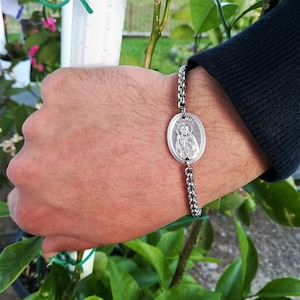 Pu&ograve; includere: Un braccialetto a catena d'argento con un ciondolo rotondo d'argento che presenta una figura religiosa. Il ciondolo ha la scritta "Jude" incisa.
