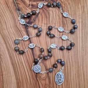 May include: A brown wooden rosary with silver beads and medallions. The medallions feature religious imagery. The rosary is laid out on a wooden surface.