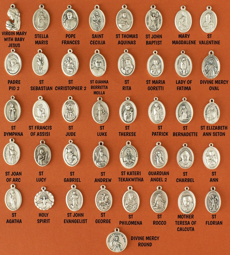 May include: A collection of silver oval-shaped medallions with various religious figures and names. The medallions are arranged in rows on a brown background.