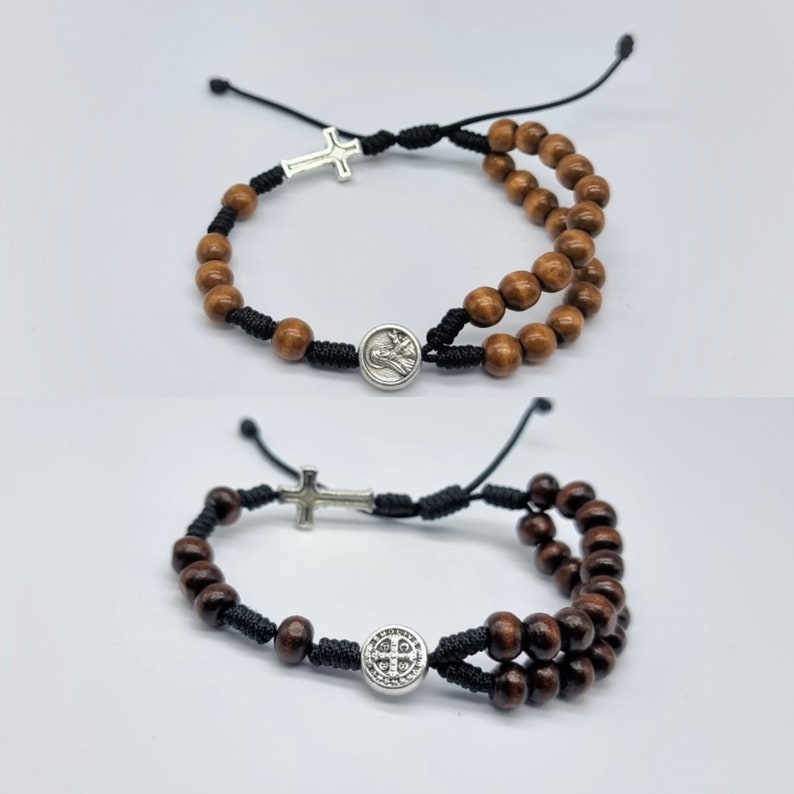 May include: Two brown wooden bead bracelets with black string and silver charms. One bracelet has a cross charm and the other has a round charm with a design.