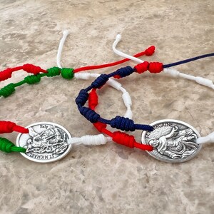 May include: Three knotted bracelets with religious medallions. The bracelets are red, white and blue, and the medallions feature images of St Michael and St Peregrine.