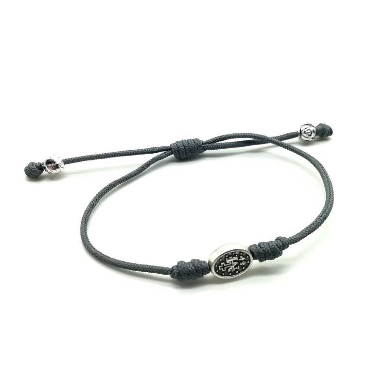 May include: A gray cord bracelet with a silver oval charm featuring a black and white design. The charm has a knot on each side.