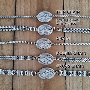 May include: Five silver bracelets with a religious pendant featuring the image of Saint Peregrine. The bracelets feature different chain styles, including thin chain, double chain with cross, chain, double chain, and cross chain.