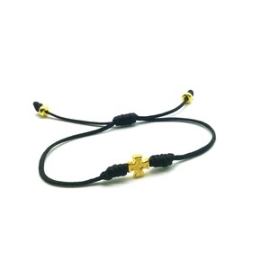 May include: A black cord bracelet with a gold cross charm. The bracelet is adjustable and can be worn by people of all ages.