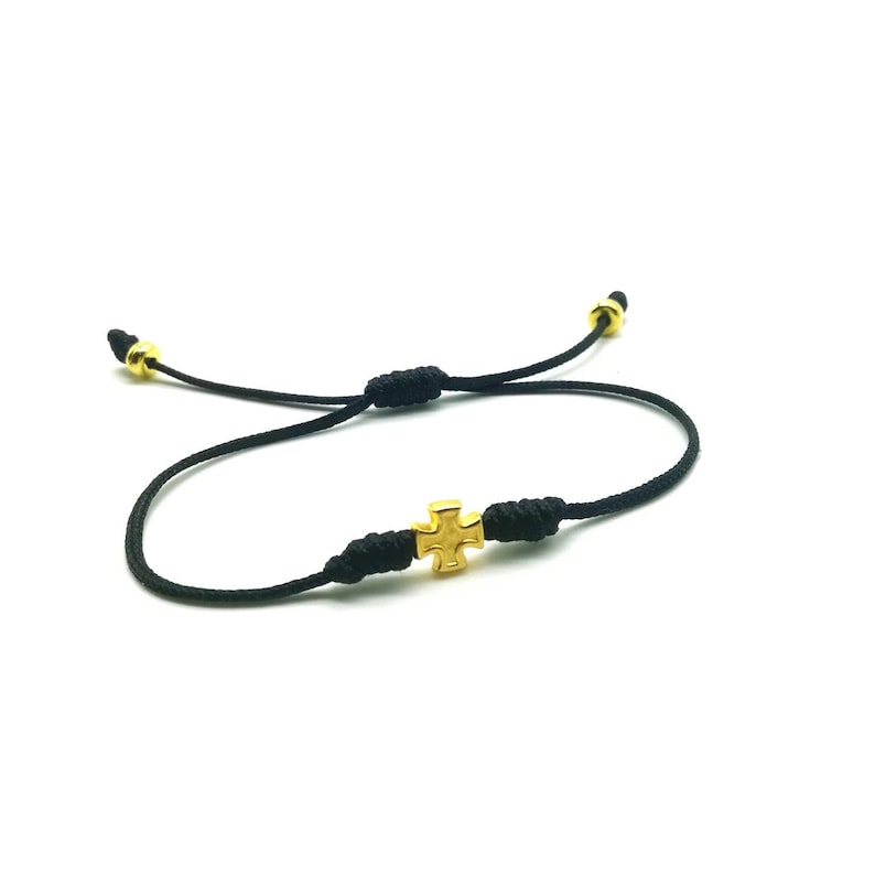 May include: A black cord bracelet with a gold cross charm. The bracelet is adjustable and can be worn by people of all ages.