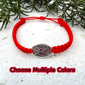 Puede incluir: Pulsera de macram&eacute; roja con un dije ovalado plateado con una imagen religiosa y el texto "Italy" y "St. Michael". La pulsera tiene un cierre de nudo corredizo. Se muestra el texto "Choose Multiple Colors".