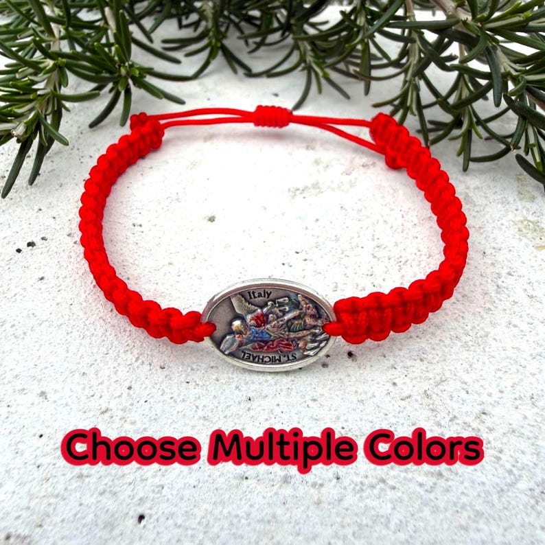 Puede incluir: Pulsera de macram&eacute; roja con un dije ovalado plateado con una imagen religiosa y el texto "Italy" y "St. Michael". La pulsera tiene un cierre de nudo corredizo. Se muestra el texto "Choose Multiple Colors".