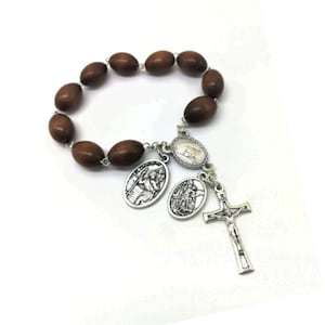May include: A brown wooden rosary bracelet with silver charms featuring religious figures. The bracelet has a silver cross with a figure of Jesus Christ.