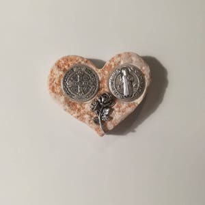 K&ouml;nnte beinhalten: Ein herzf&ouml;rmiger Stein mit einer silbernen St. Christopher-Medaille und einer silbernen St. Benedikt-Medaille sowie einer silbernen Rose.
