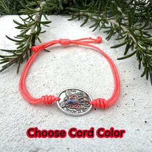 Puede incluir: Una pulsera de color coral con un colgante ovalado plateado que presenta una imagen de San Miguel y la palabra "Italia". La pulsera est&aacute; hecha de cord&oacute;n tejido y tiene nudos ajustables. El texto "Choose Cord Color" es rojo.