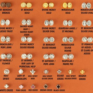May include: A collection of 20 round metal medallions with various religious figures and symbols. The medallions are arranged in rows on a brown background. The medallions are made of silver, gold, and bronze. The text on the medallions includes names like St. Benedict, Divine Mercy, and Miraculous.