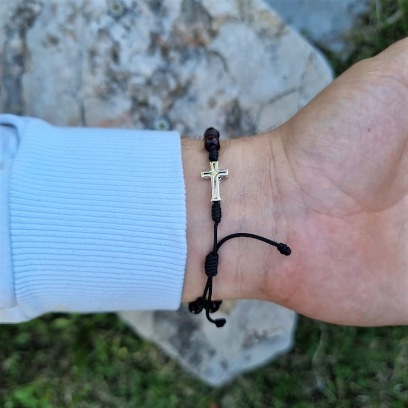 May include: A black cord bracelet with brown wooden beads and a silver cross charm.
